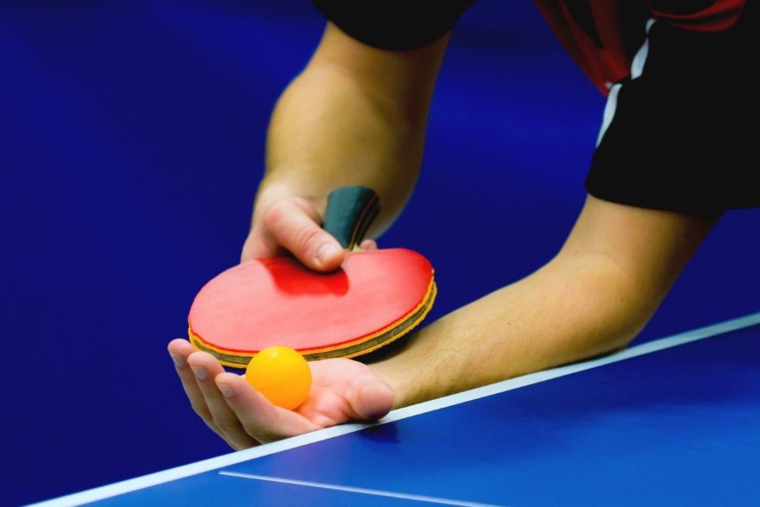 person playing table tennis serving with ball and racket
