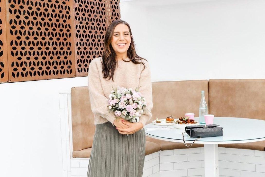woman standing in the avenue cafe in front of coffee table holding flowers with coffee and food behind her