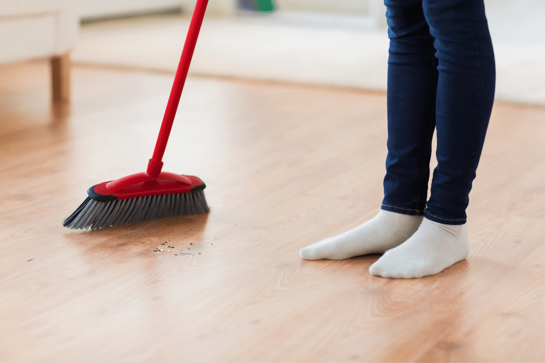A woman sweeps the floor with a broom.