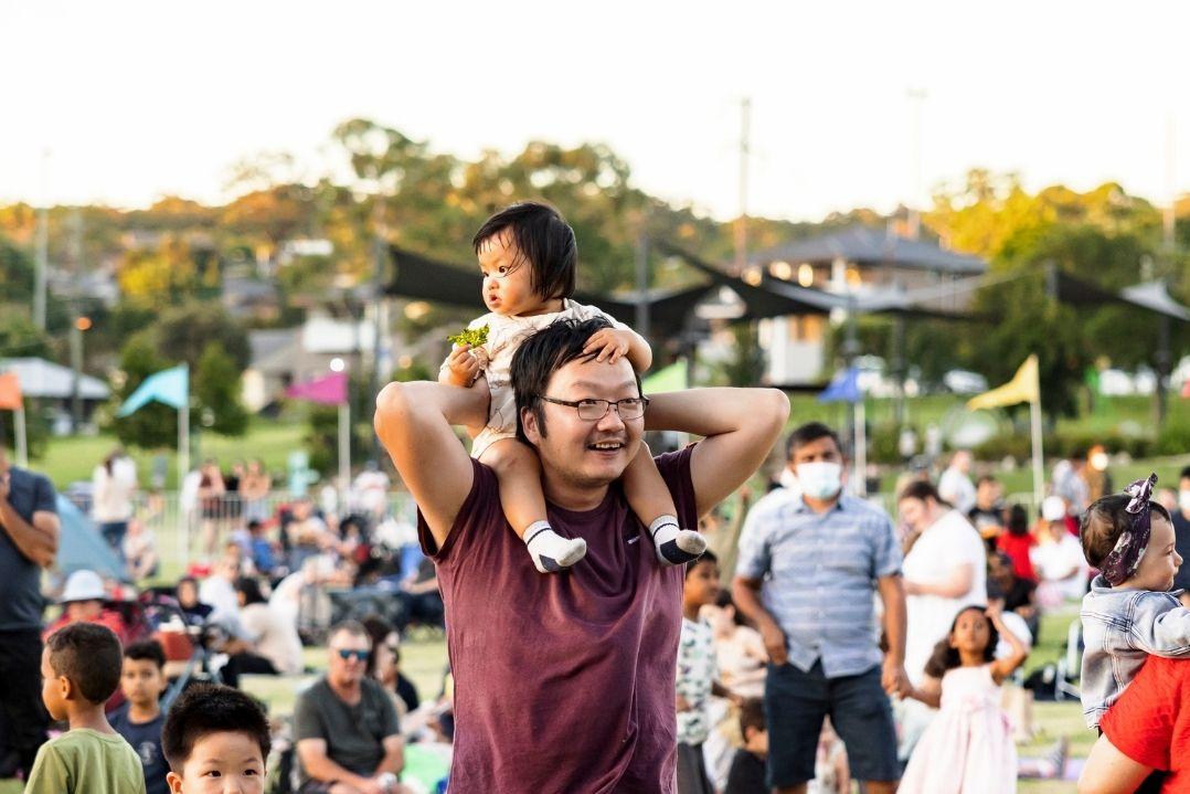 A dad with his child on his shoulders amongst a crowd of people at a Parramatta event.