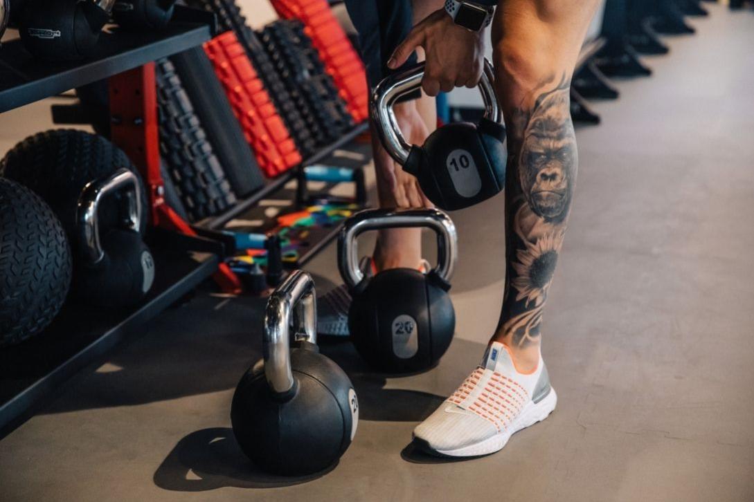 man with leg tattoo picking up weights