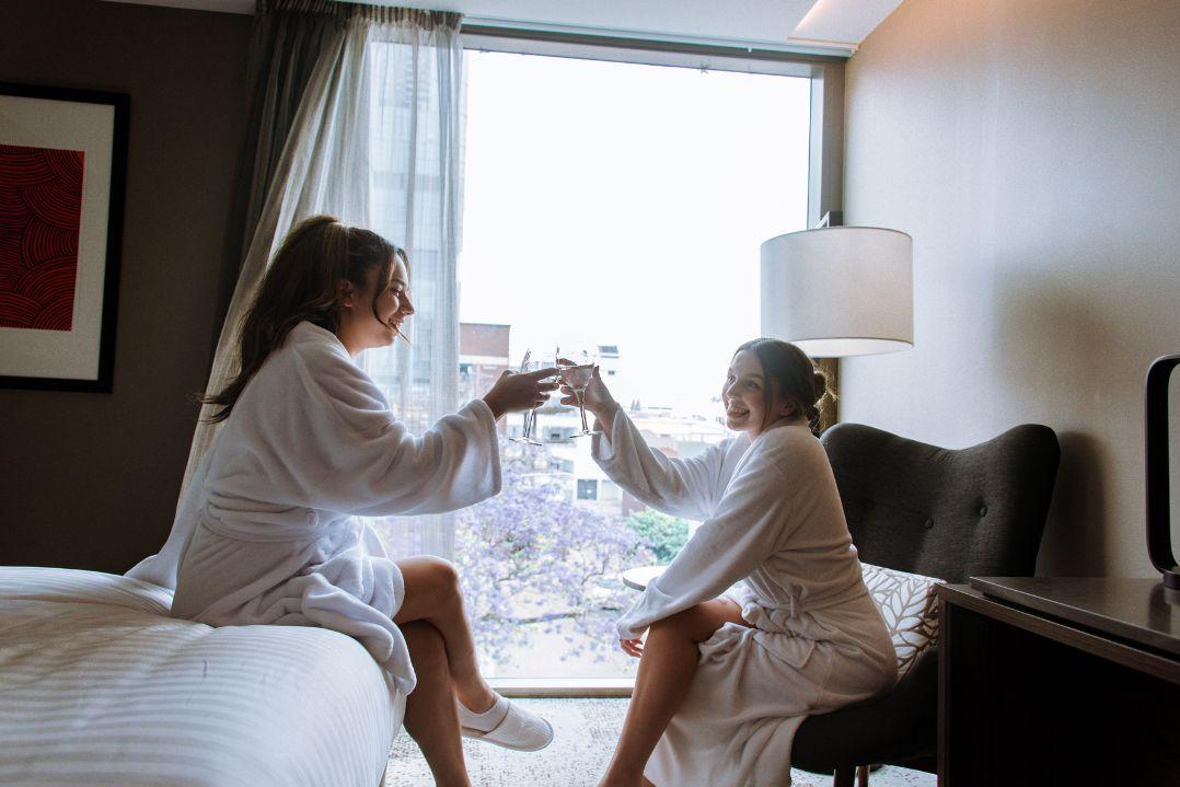 two friends cheersing champagne in hotel bath robes in a hotel room