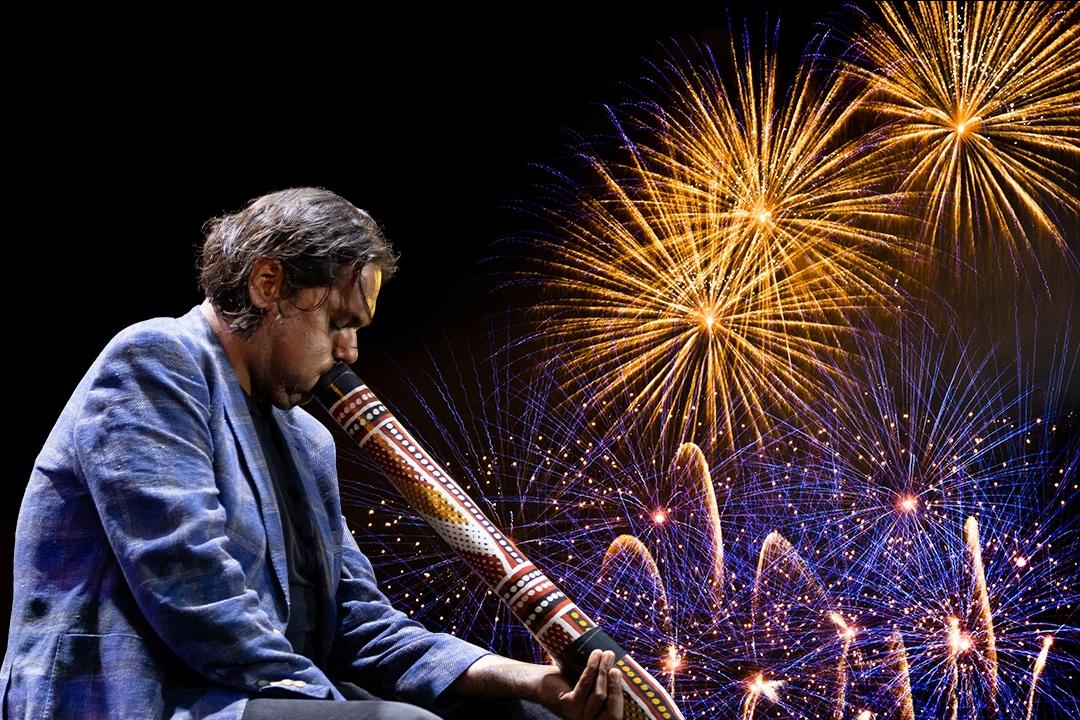 Man playing a didgeridoo infront of fireworks