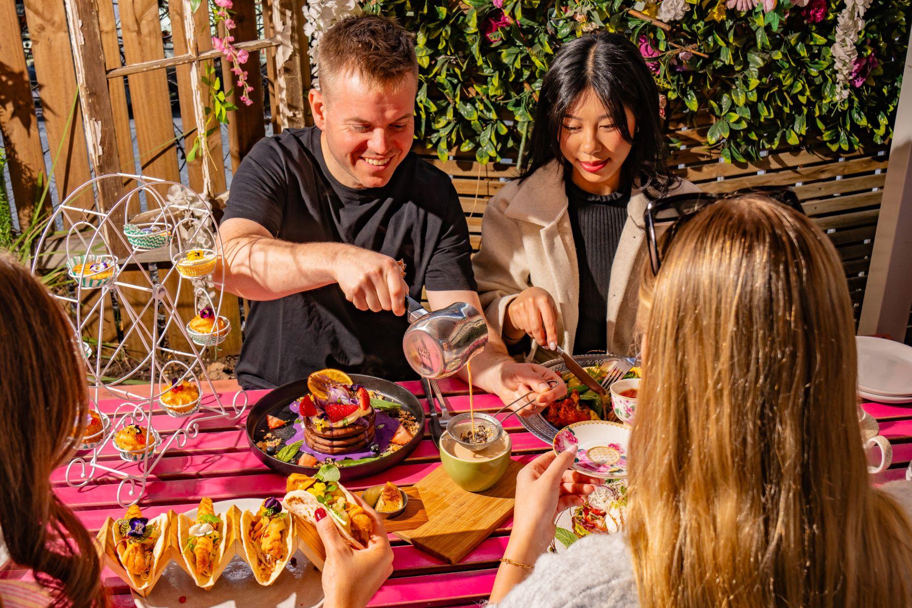 Group of people eating food and having drink son a pink table