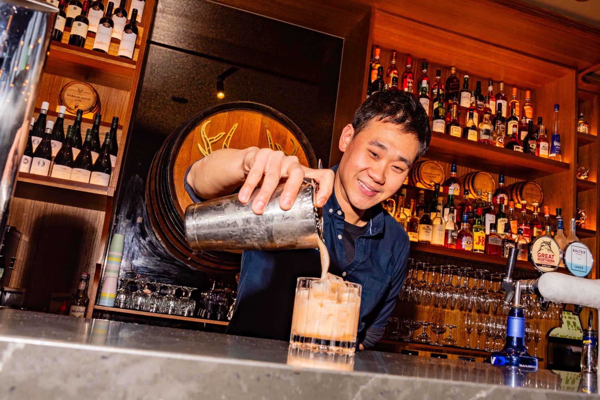 Man at a bar pouring a cocktail