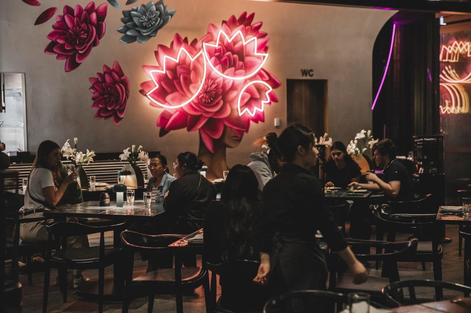 People sitting in a restaurant, bright pink neon sign on the wall