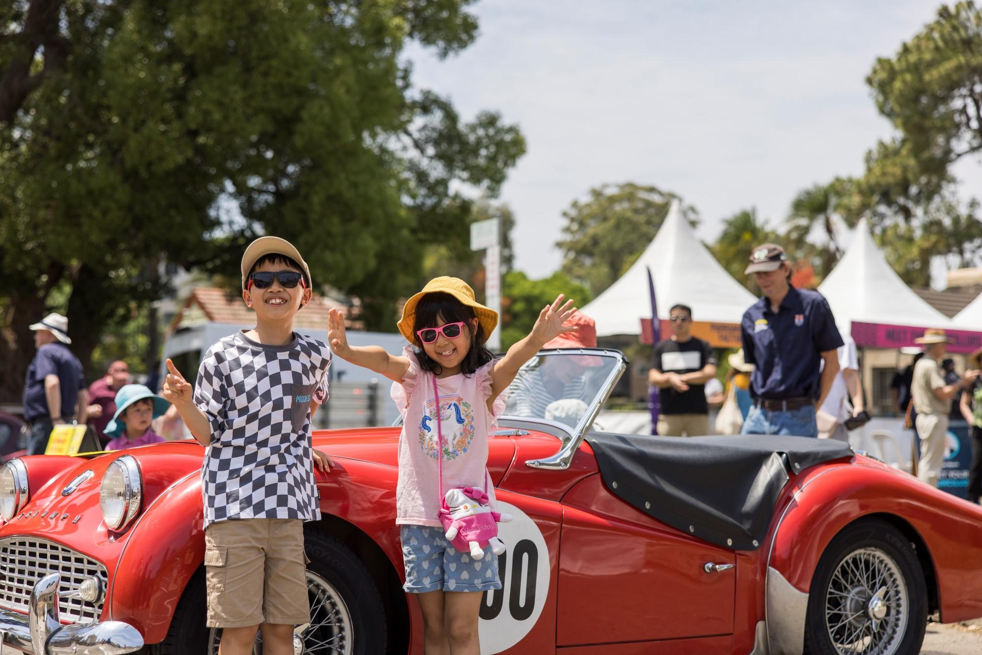 Two happy kids smiling standing in front of retro car