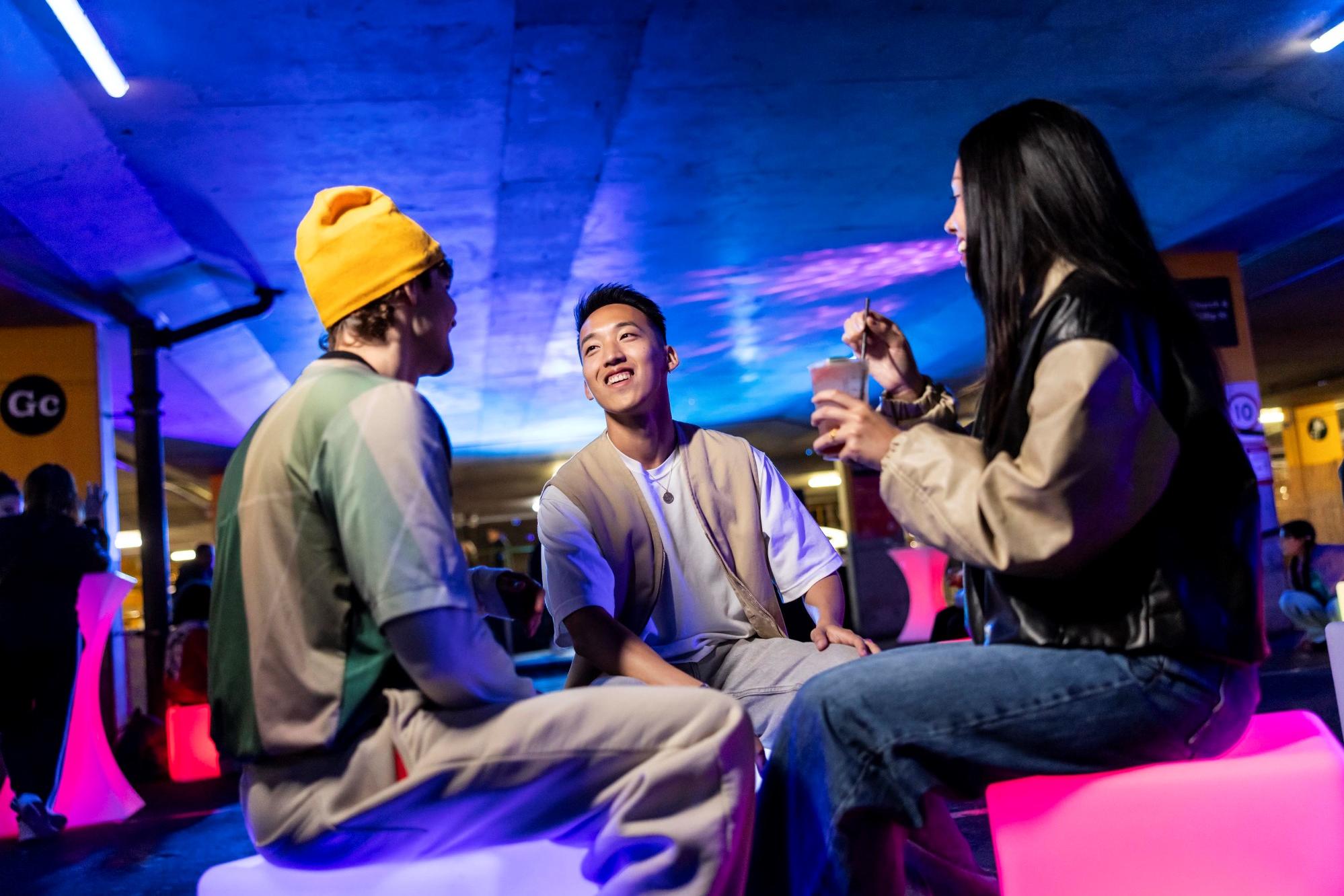 Three happy people sitting down surrounded by blue & purple lights