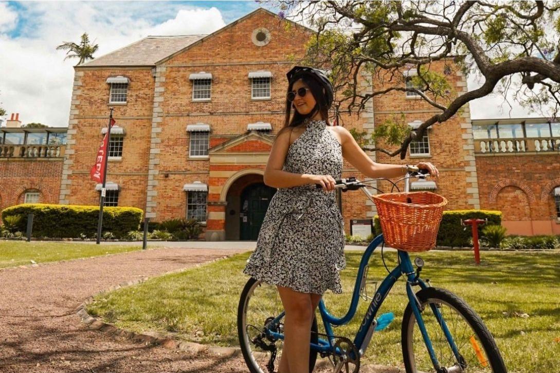 girl holding the handlebars of a bike with a wicker basket in front of the Whitlam Institute Parramatta