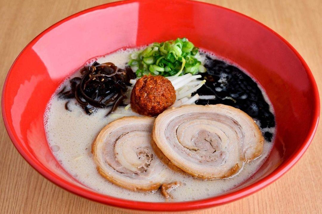 Large red bowl of ramen with cloudy stock and thin slices of meat