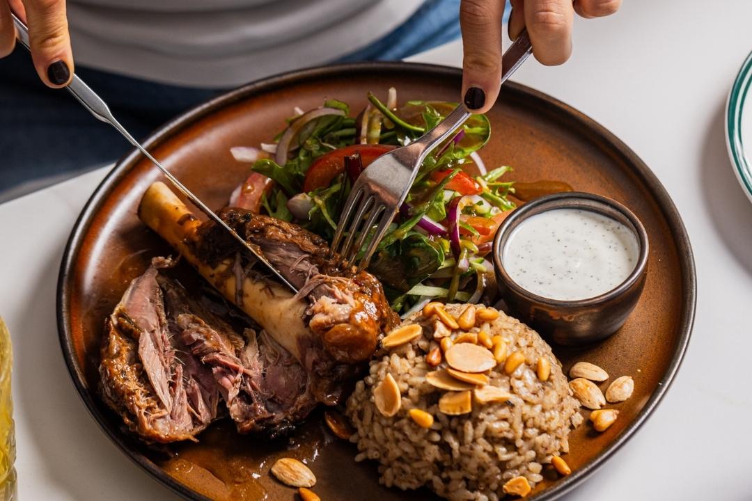 Knife and fork cutting soft lamb off the bone