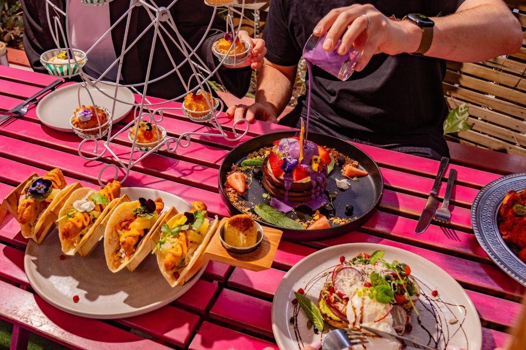 Pink table with delicious tacos and pancakes