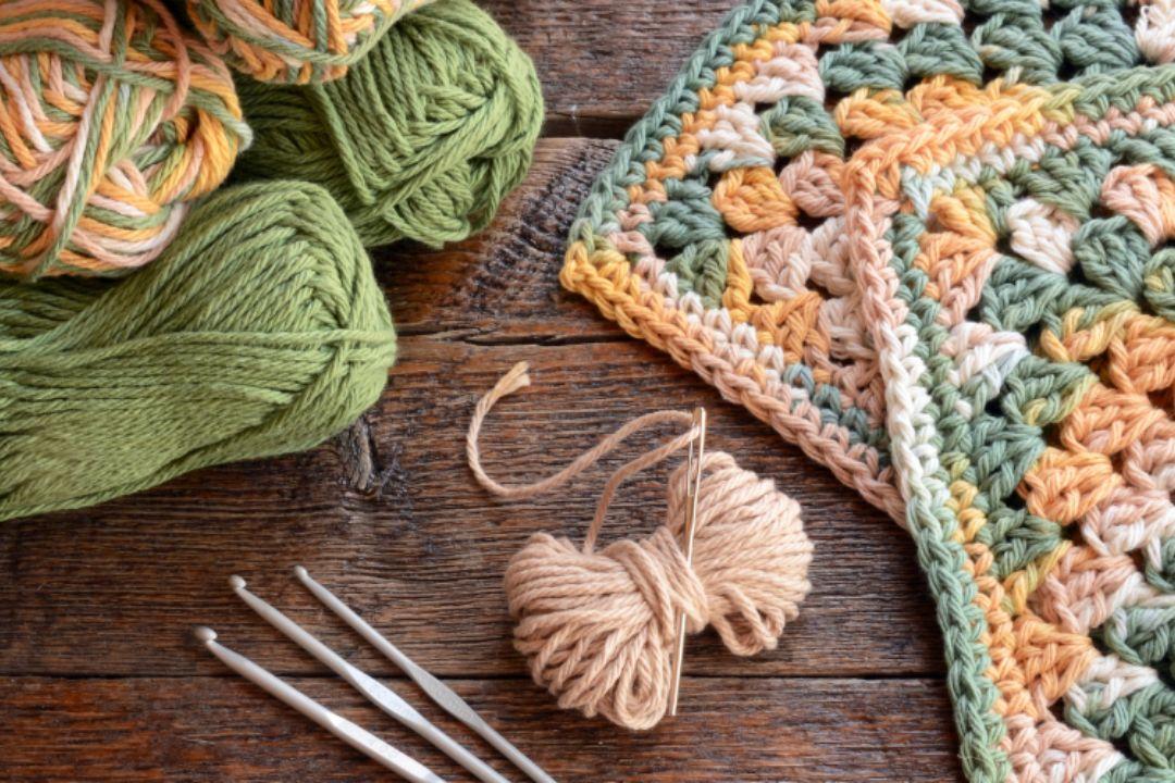 Green wool yan with knitting needles and then a needle square
