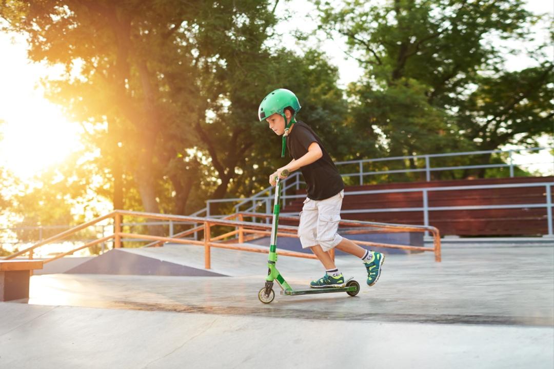 A boy on a scooter and in protective helmet do incredible stunts in skate park