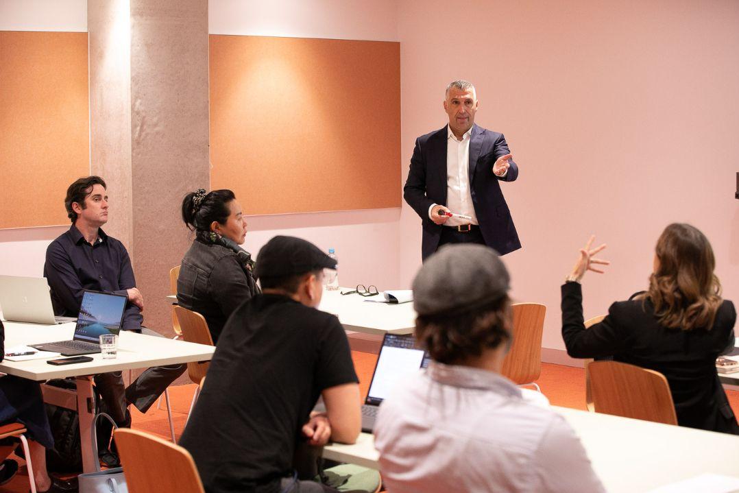 Man standing in front of small room of people giving presentation