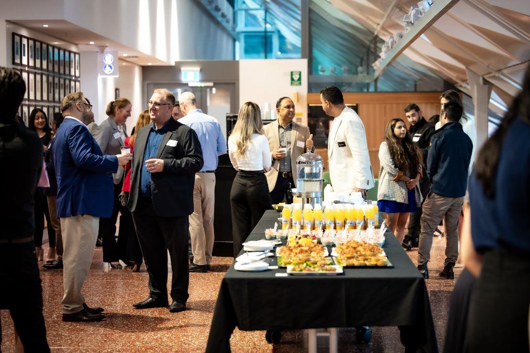 A room full of people in suits talking around a table of canapes and drink glasses