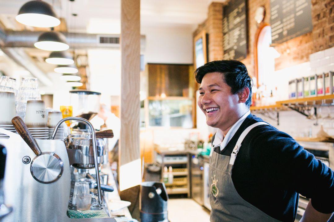 Man smiling wearing apron standing in front of coffee maker