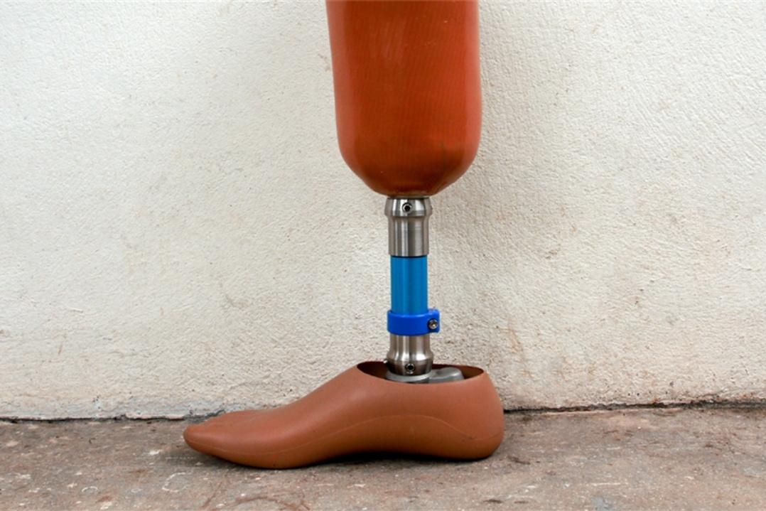 A prosthetic leg with a wooden foot and metallic joints stands against a plain white wall. The image conveys resilience and advancement in prosthetics.