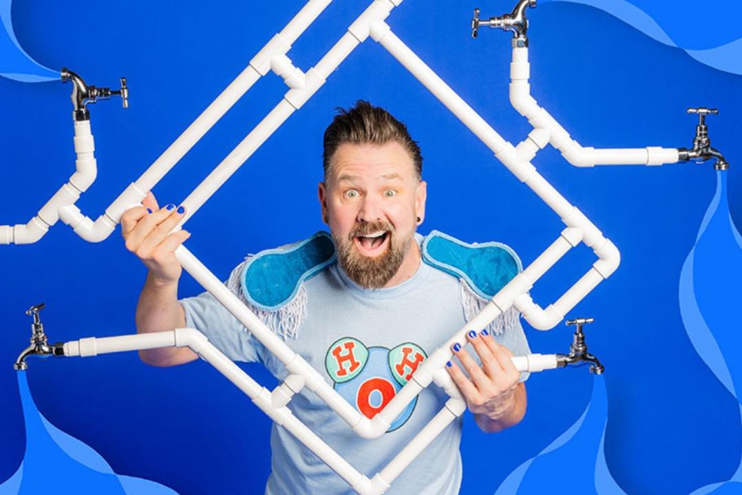 A man with a surprised expression holds white plumbing pipes against a vibrant blue geometric background, conveying creativity and excitement.