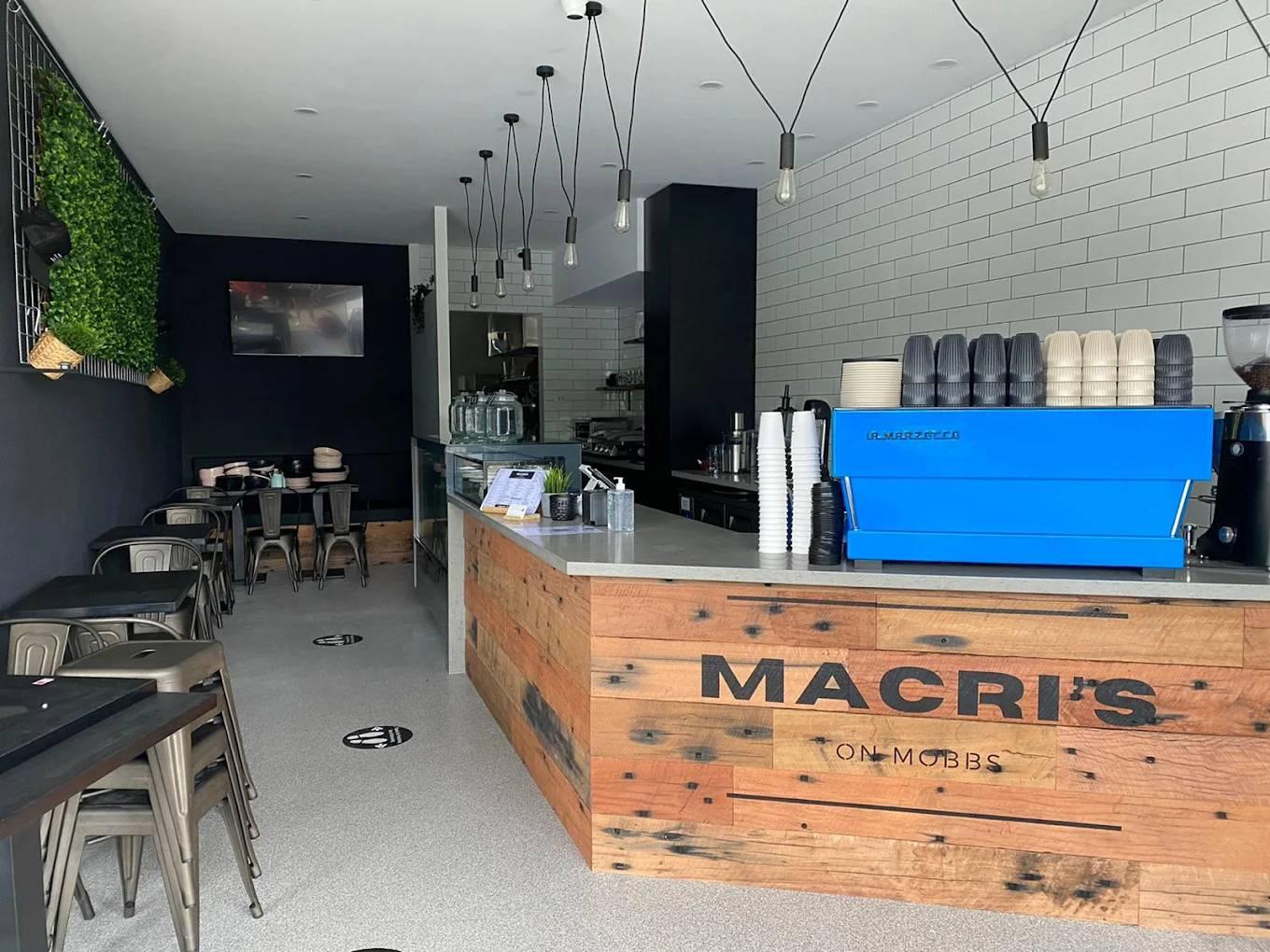 Modern cafe interior with wooden counter labeled "Macri's," featuring a blue coffee machine.