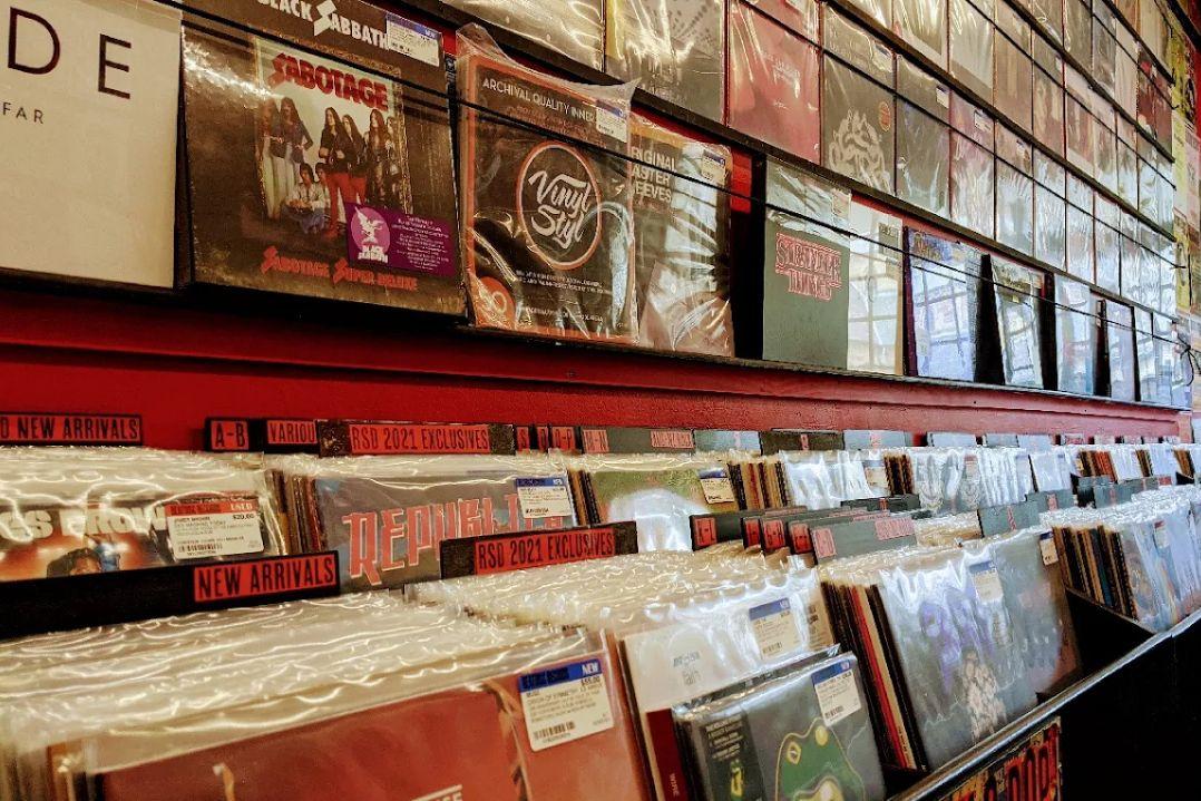 Vinyl records neatly displayed on red shelves, with colorful album covers and signs labeled "New Arrivals." The scene feels nostalgic and vibrant.