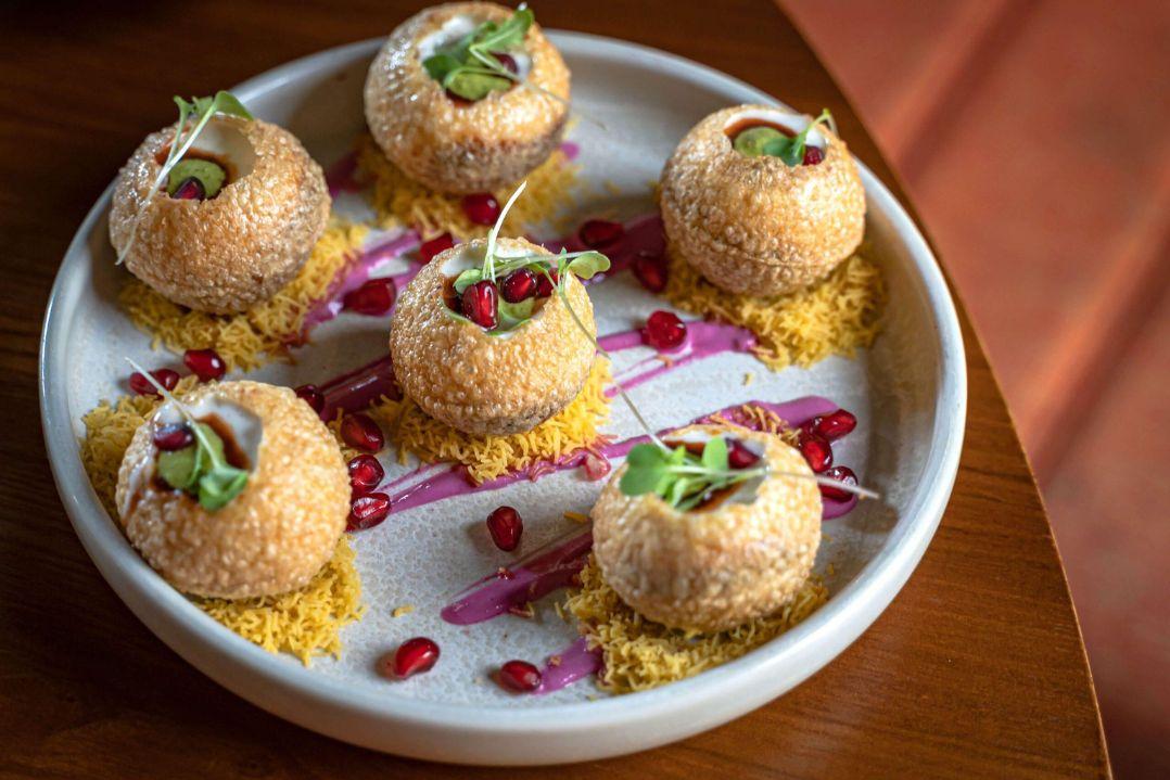 A plate of six gourmet spherical appetizers garnished with greens, placed on a decorative pink sauce swirl, exuding elegance and culinary artistry.