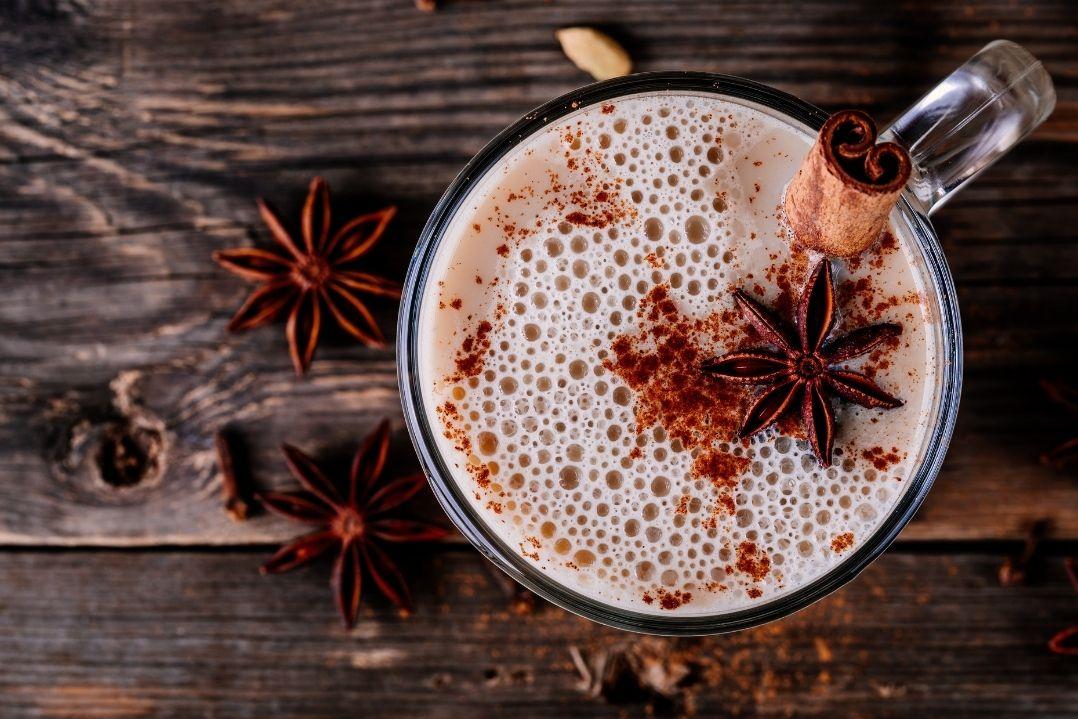 A top view of a frothy latte in a glass mug, sprinkled with cinnamon and garnished with star anise, set on a rustic wooden table with warm tones.