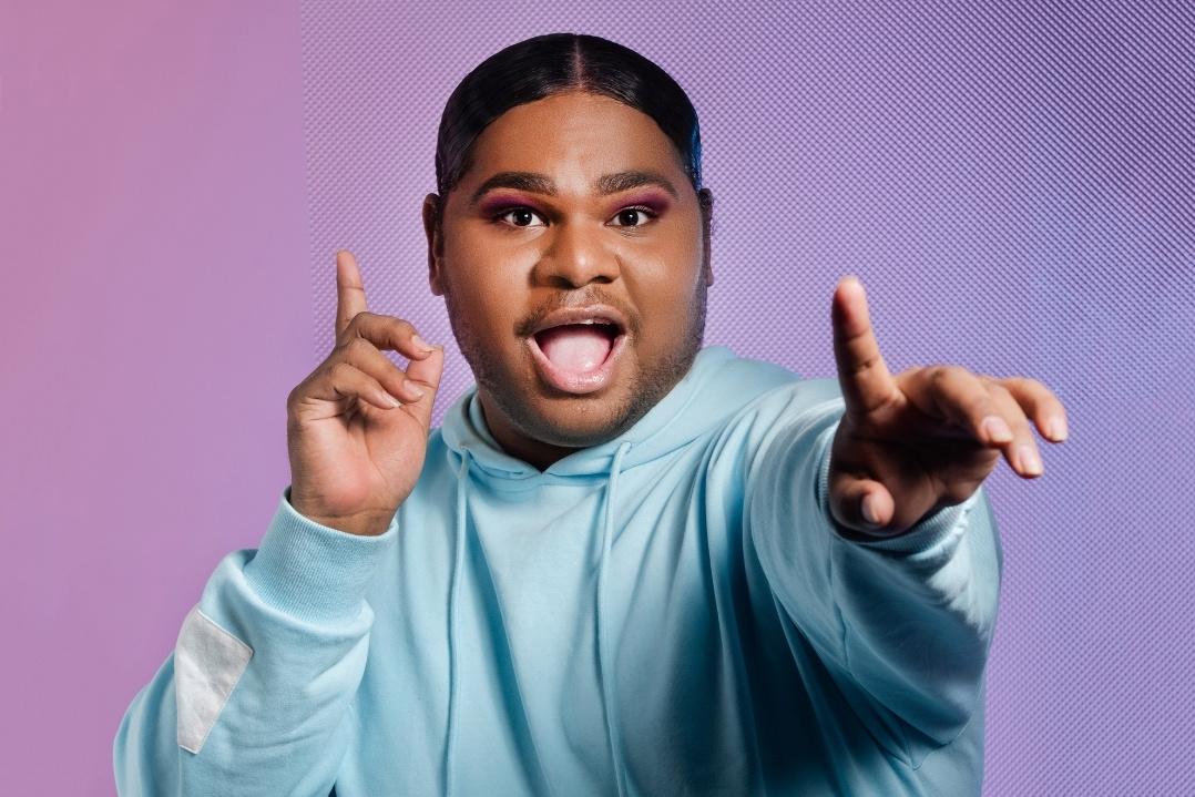 Person in a blue hoodie poses with an expressive, enthusiastic gesture against a pink and purple gradient background, conveying excitement.