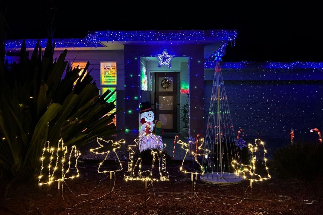 A house adorned with festive Halloween lights and decorations, featuring glowing pumpkins, a ghost figure, and purple and blue lighting, creating a spooky ambiance.