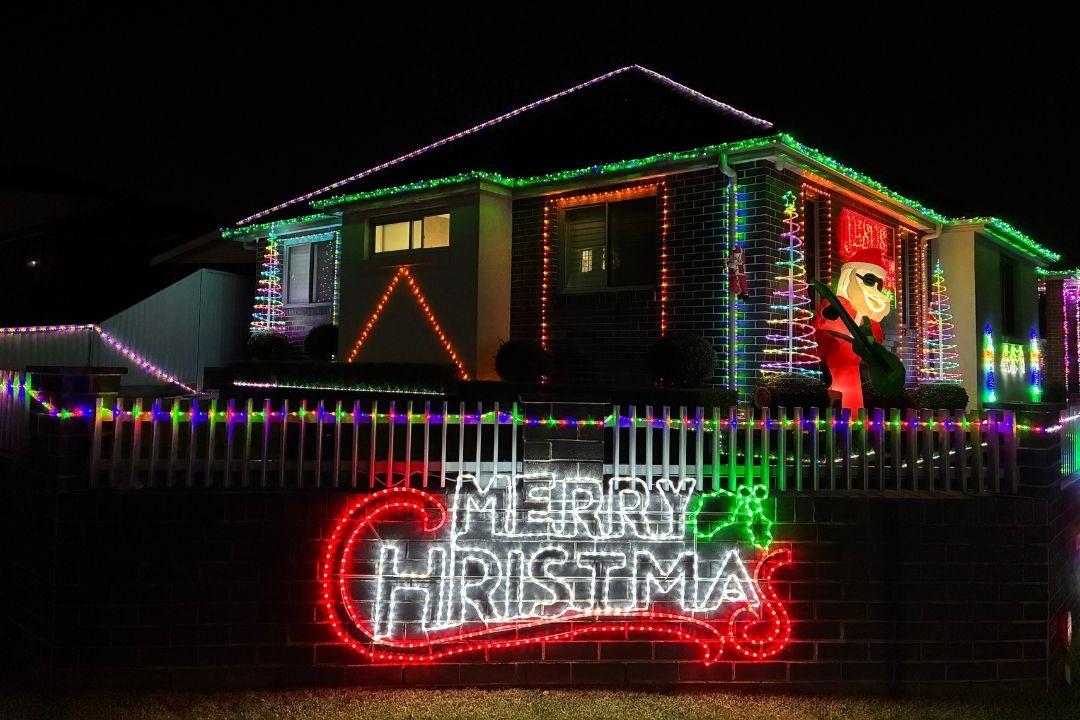 A house is decorated with vibrant Christmas lights, including a large "Merry Christmas" sign. The warm glow creates a festive holiday atmosphere.