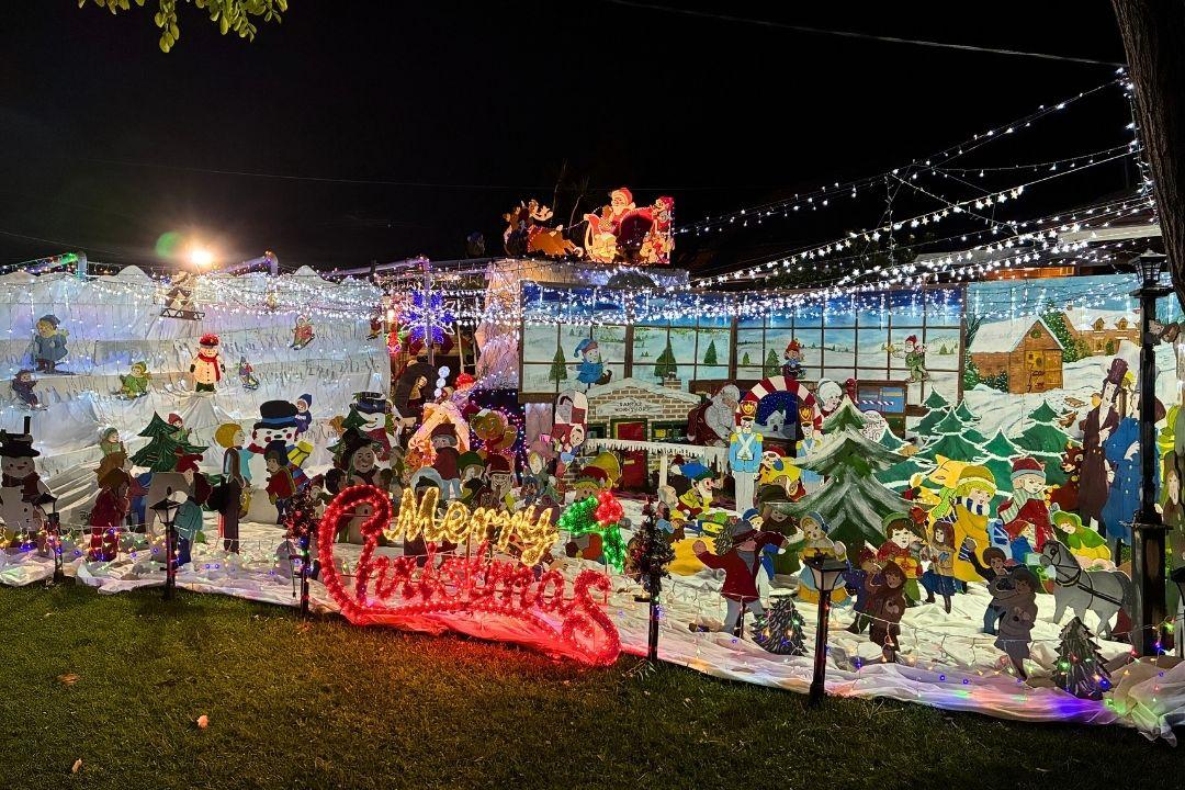Festive Christmas display with colourful lights, Santa figures, and reindeer in a yard. The scene is bright, cheerful, and full of holiday spirit.