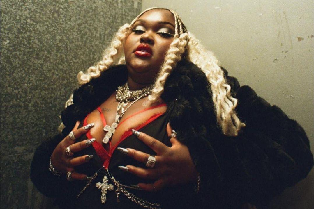 A confident person with long platinum curls and bold makeup poses in a fur coat, wearing jewellery, and exuding a fierce and powerful presence.