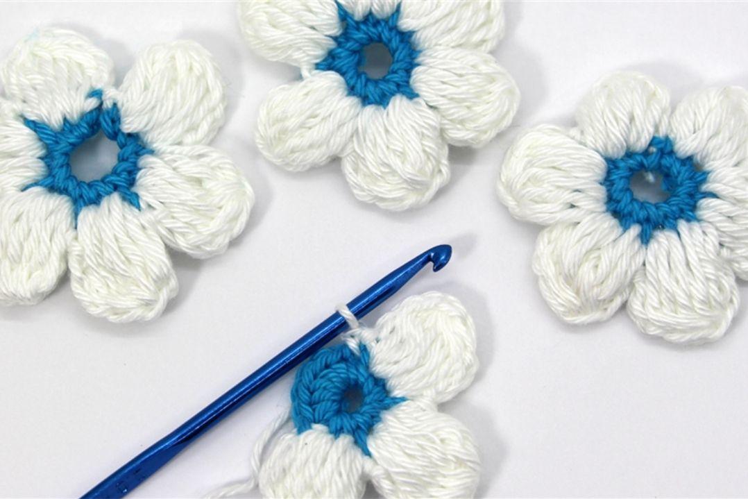 Three white flowers with intricate, textured petals and bright blue centers are arranged on a white surface. A blue pen lies diagonally across the flowers.