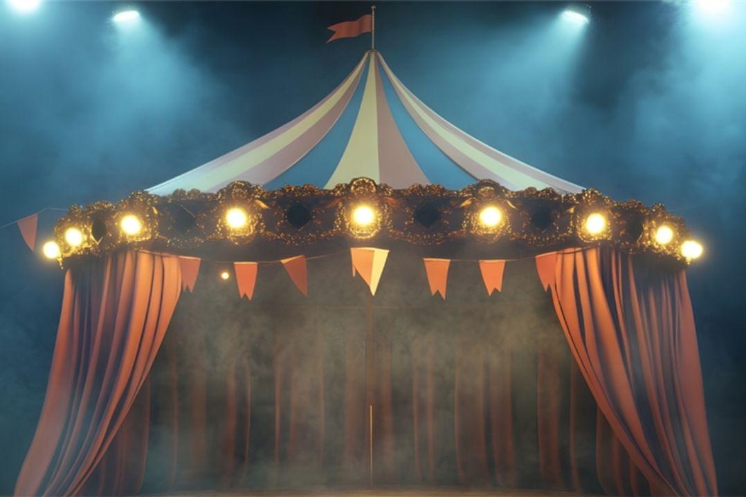 A circus tent under bright stage lights creates an atmosphere of excitement and mystery. The striped canopy is surrounded by red drapes and a haze of smoke.