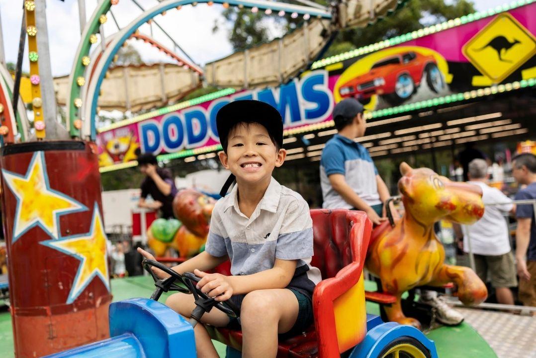 A smiling boy sits in a colourful, toy-themed amusement park ride. Creating a joyful atmosphere.