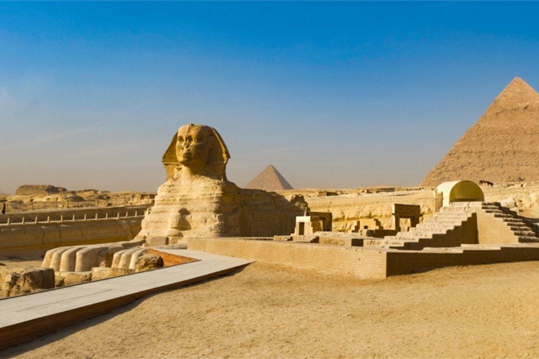 A majestic view of the Sphinx and Pyramids of Giza under a clear blue sky, set in a sandy desert landscape, conveying ancient history and grandeur.