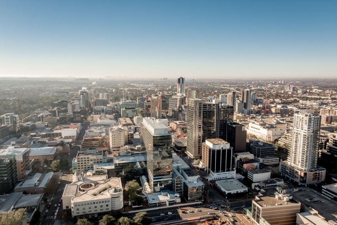 Aerial view of a sprawling cityscape with tall skyscrapers and densely packed buildings under a clear blue sky, conveying a sense of urban bustle.