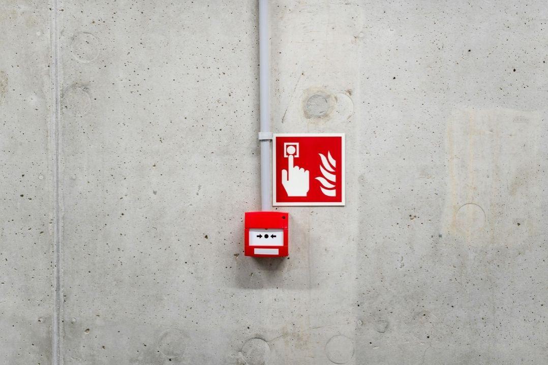A red fire alarm and sign with a fire extinguisher symbol are mounted on a gray concrete wall, highlighting emergency safety equipment in a minimalist setting.