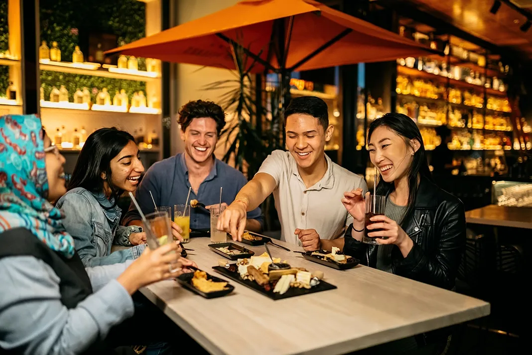 A group of five people laughing and sharing food at a restaurant table.