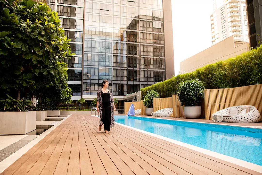 Woman in a long black dress walks along a modern rooftop pool deck.