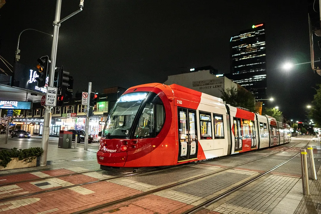 A red and white tram travels along a city street at night, illuminated by streetlights.