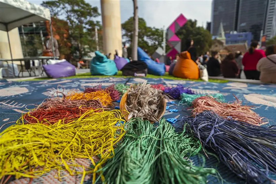 A person joyfully surrounded by piles of colorful confetti in shades of yellow, orange, green, and blue, with trees and people in the background.