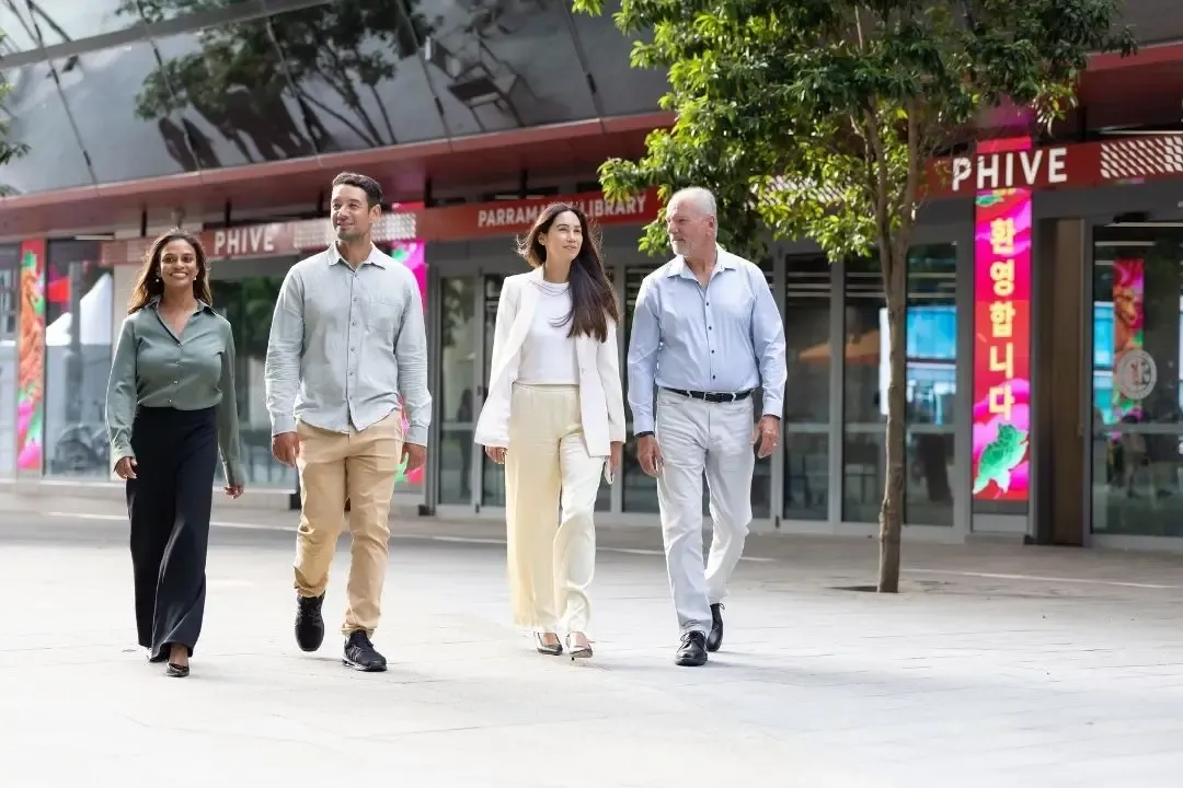 Four people, dressed in business casual, walk confidently outside a modern building with "PHIVE" signs.