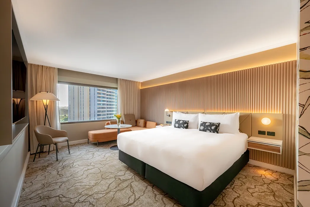 Modern hotel room with a large, neatly made bed, soft lighting, and stylish decor.