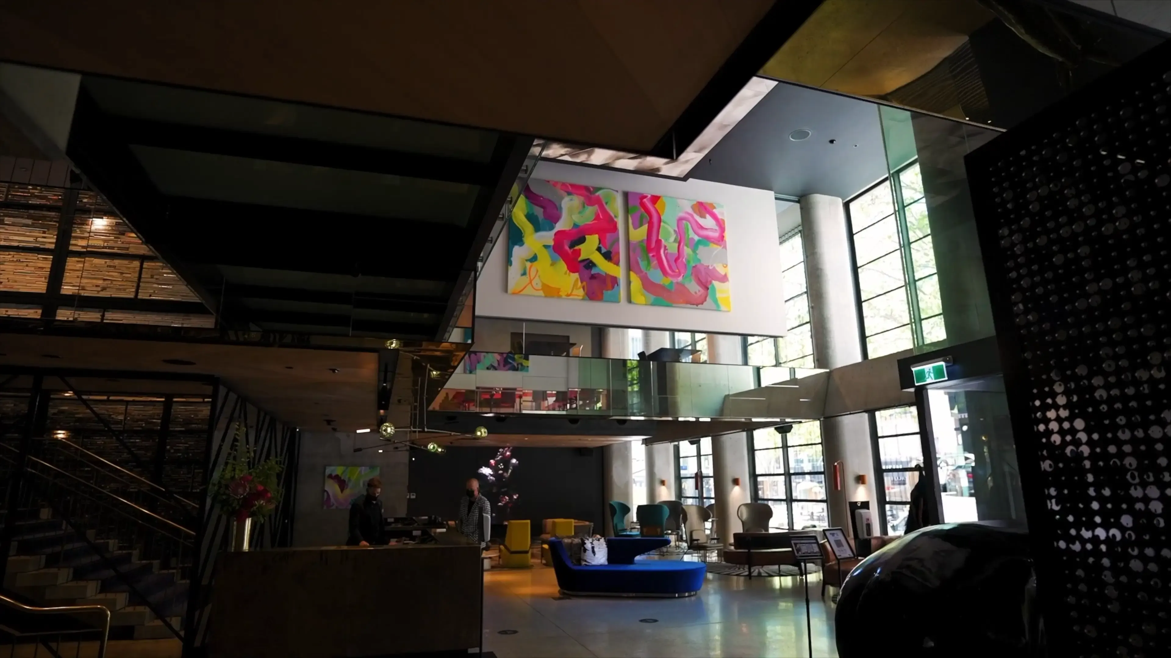 A modern hotel lobby with vibrant abstract art above, featuring bright colors. The space includes sleek furniture, large windows, and a welcoming atmosphere.