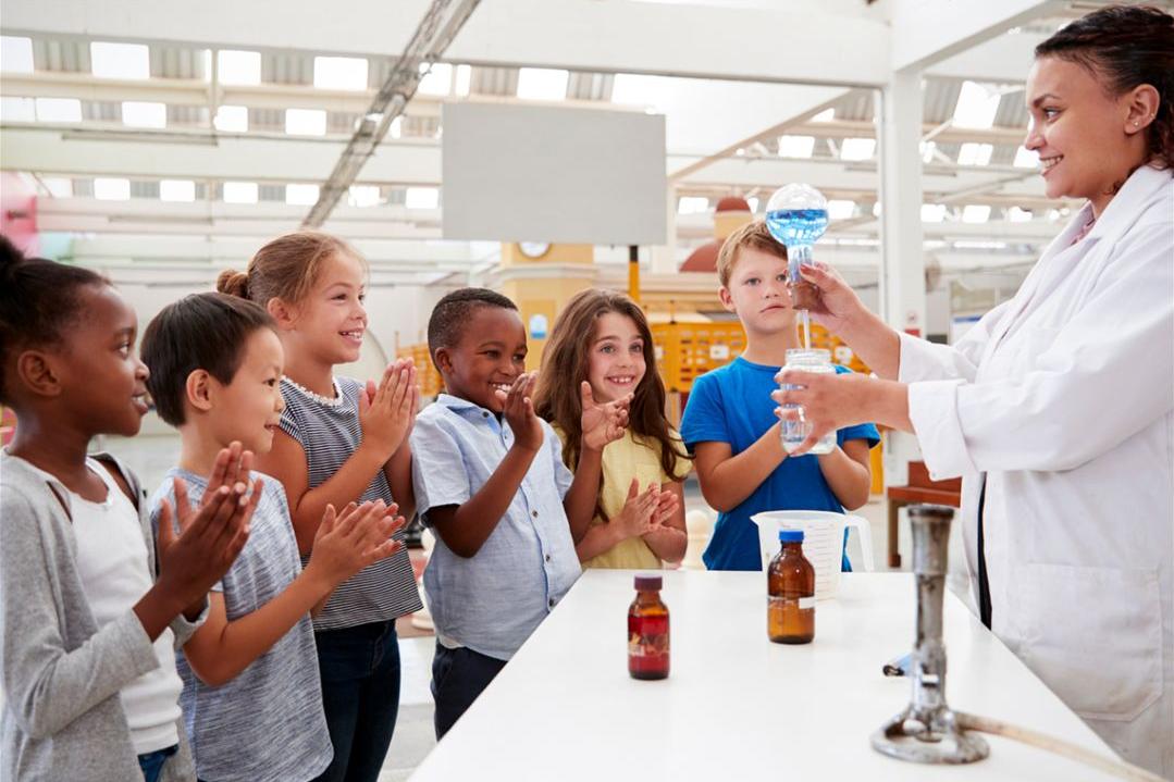Lady in white lab coat with children doing lab experiments