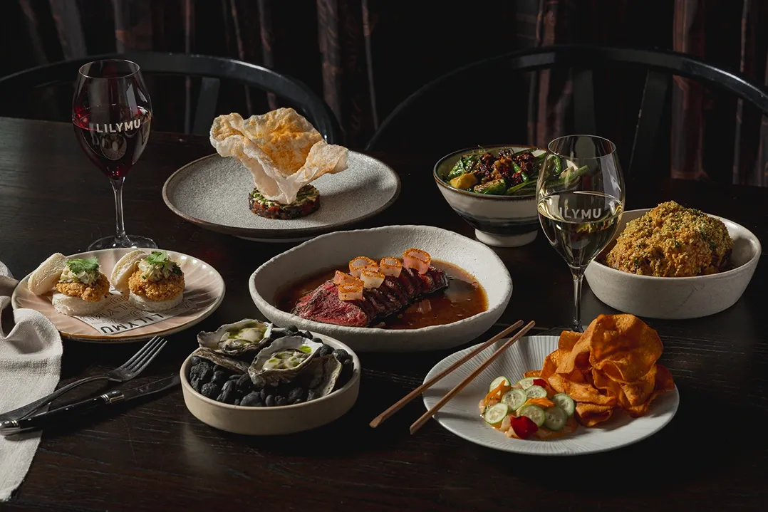 A luxurious dining table with diverse dishes: sliced steak, crispy chips, oysters, and greens, paired with red and white wine glasses, conveying elegance.