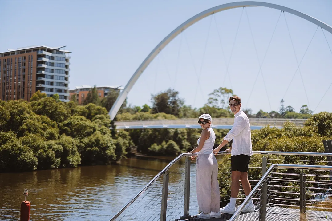 A young couple standing on a bridge looking back smiling at the camera