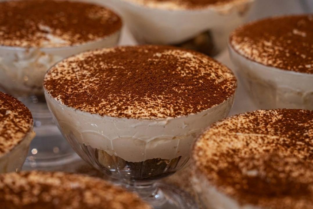 Creamy tiramisu servings in glass bowls, topped with a dusting of cocoa powder. The dessert looks rich and appetizing, evoking a sense of indulgence.