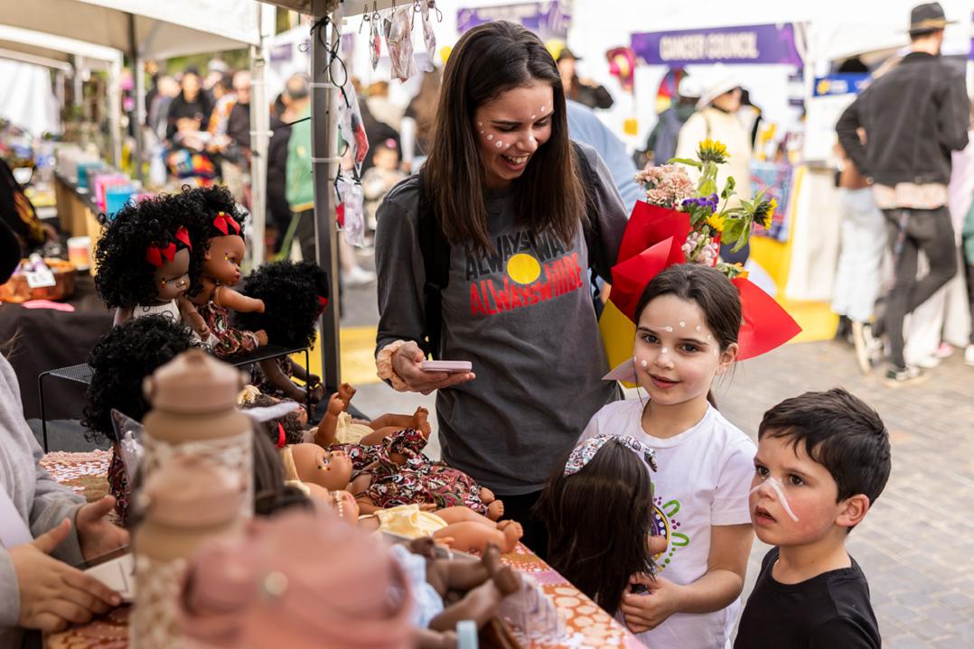 Woman smiling at kids standing next to her in front of a stall